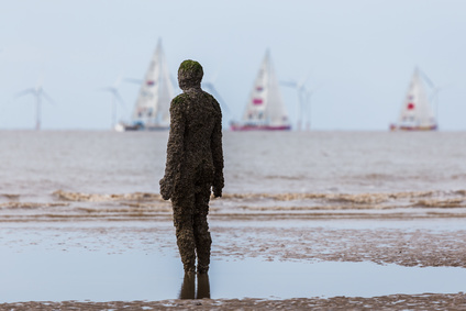 An Iron Man watches the start of the 2017/18 round the world Clipper race on a beach near Liverpool. The Clipper Race (now in its eleventh year) sees twelve global teams compete in a 40000 nautical mile around the world race on a 70 foot ocean racing yachts. The teams left the host port of Liverpool on 20 August 2017 to begin their first leg – a 5200 mile mile journey lasting approximately 33 days to South America, taking in the Canary Islands & Doldrums along the way.