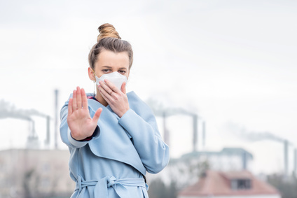 Young woman in protective mask suffering from air pollution from big manufacturing in the city