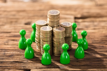 Stack Of Coins Surrounded With Green Figures On Wooden Desk